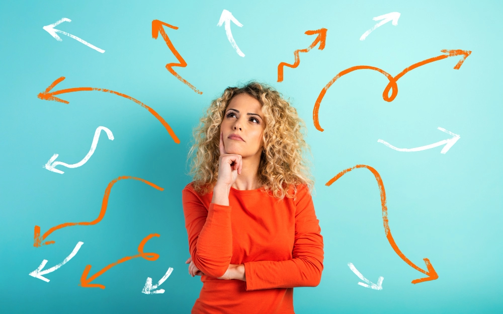Thoughtful woman standing against a blue background with various white and orange arrows pointing in different directions, symbolizing decision-making or confusion.